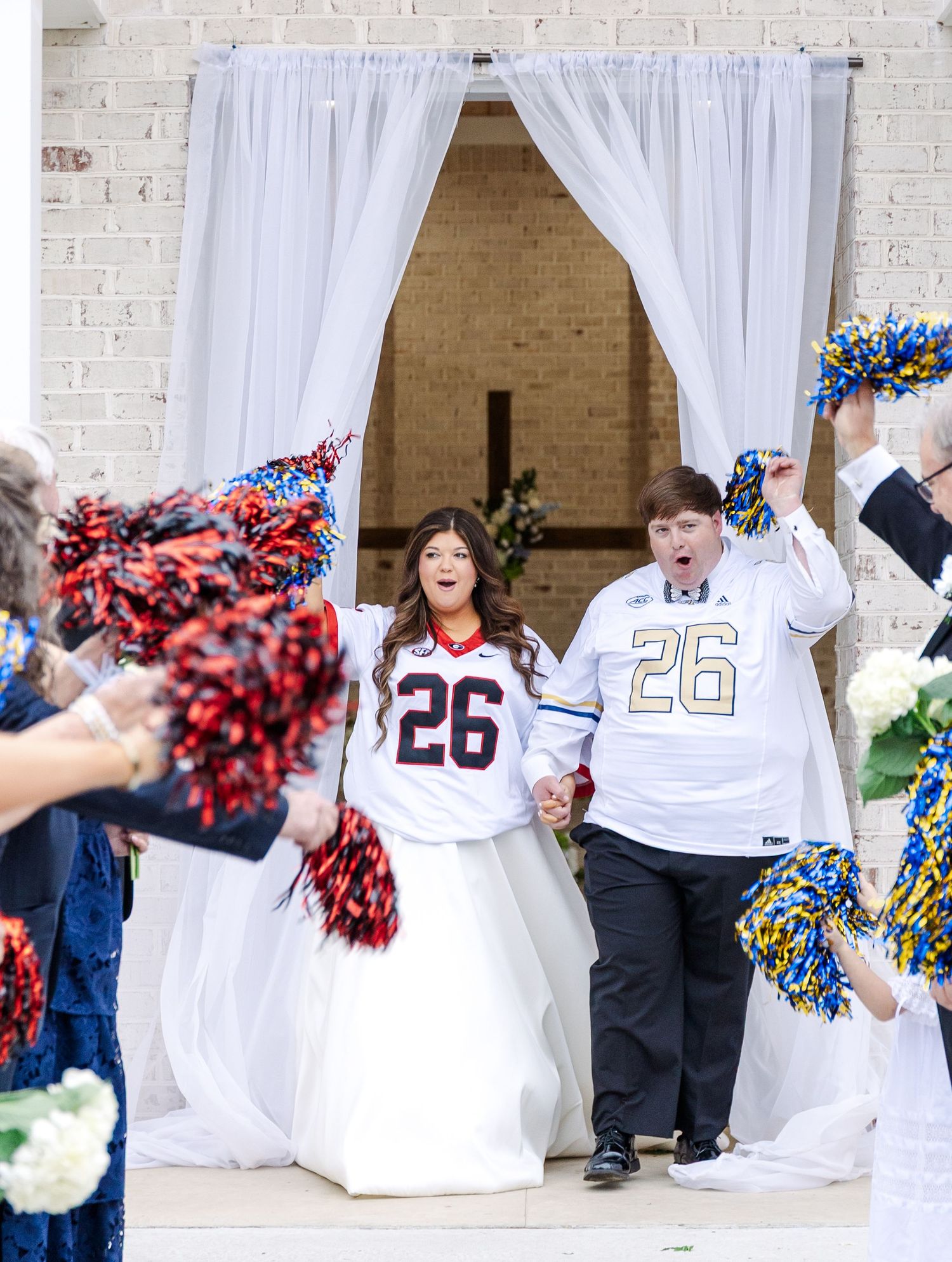 Bride and groom wearing matching number 26 football jerseys over wedding attire during fun ceremony recessional exit.