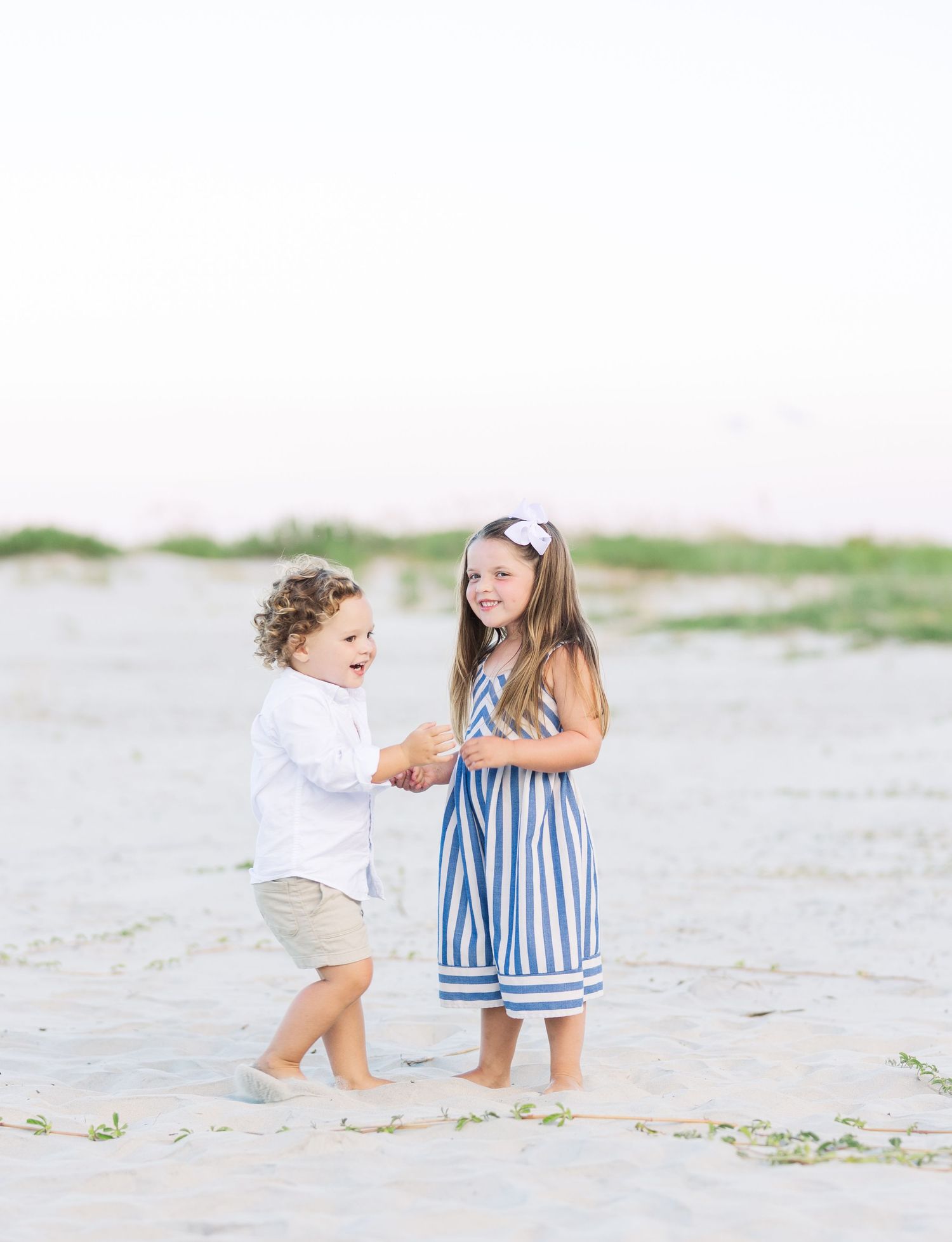Two children laugh and play together on a breezy beach.