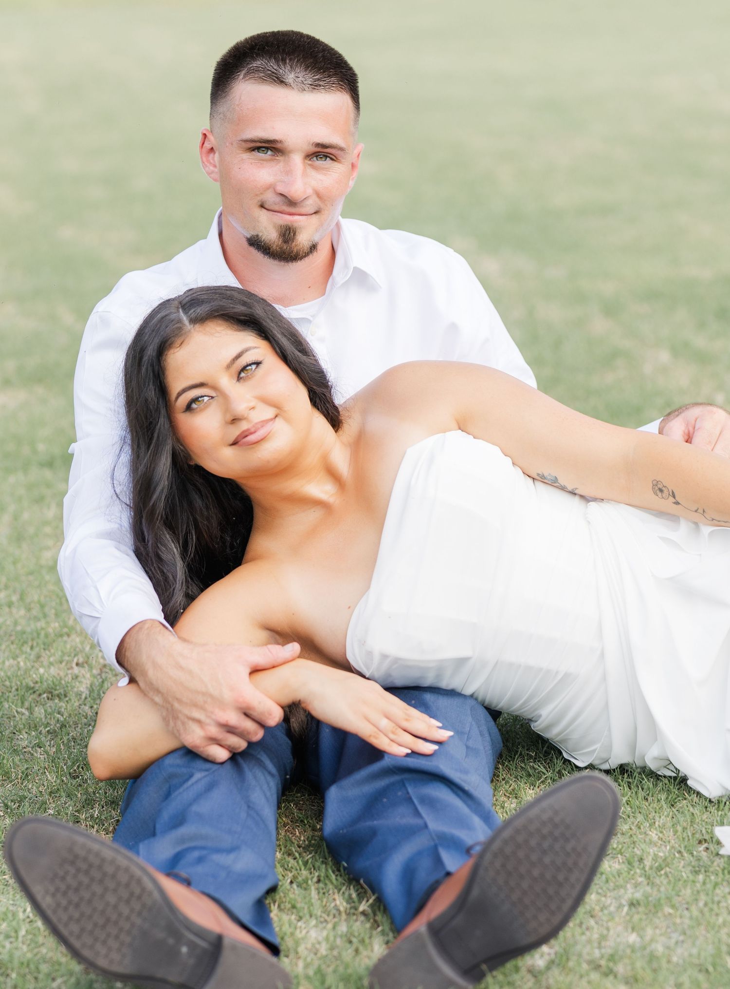 Couple relaxing on green grass, woman leaning against man in white shirt and blue jeans.