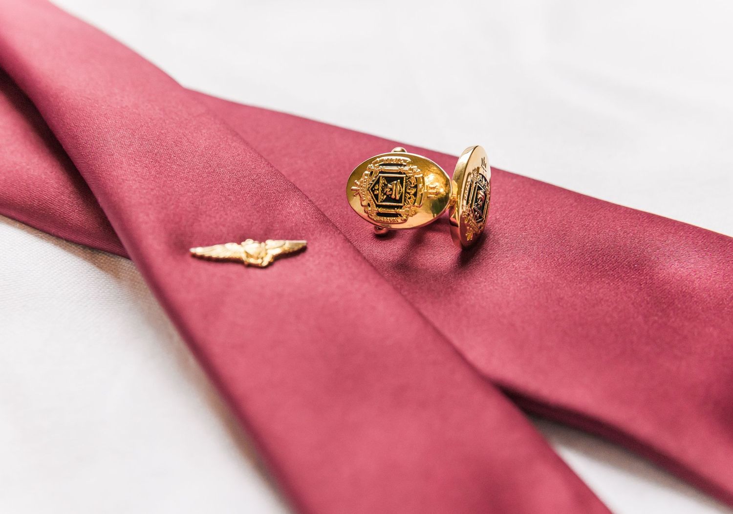 Gold rose pin and wing pin displayed on burgundy silk fabric.