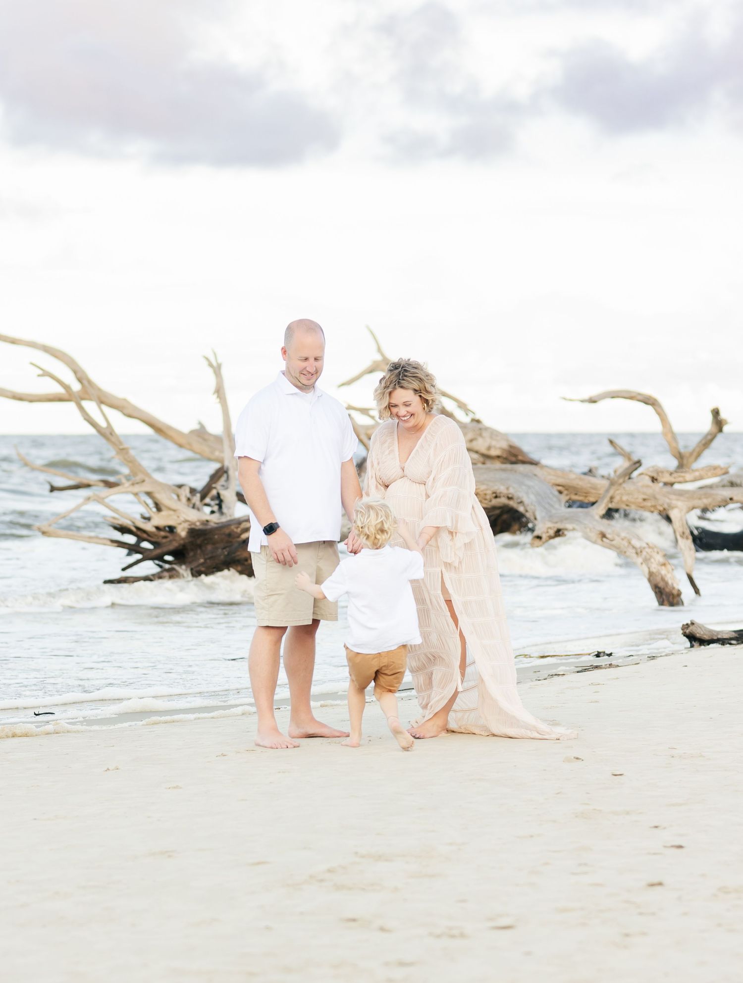 Light and airy beach maternity session with driftwood and waves creating dreamy coastal backdrop.