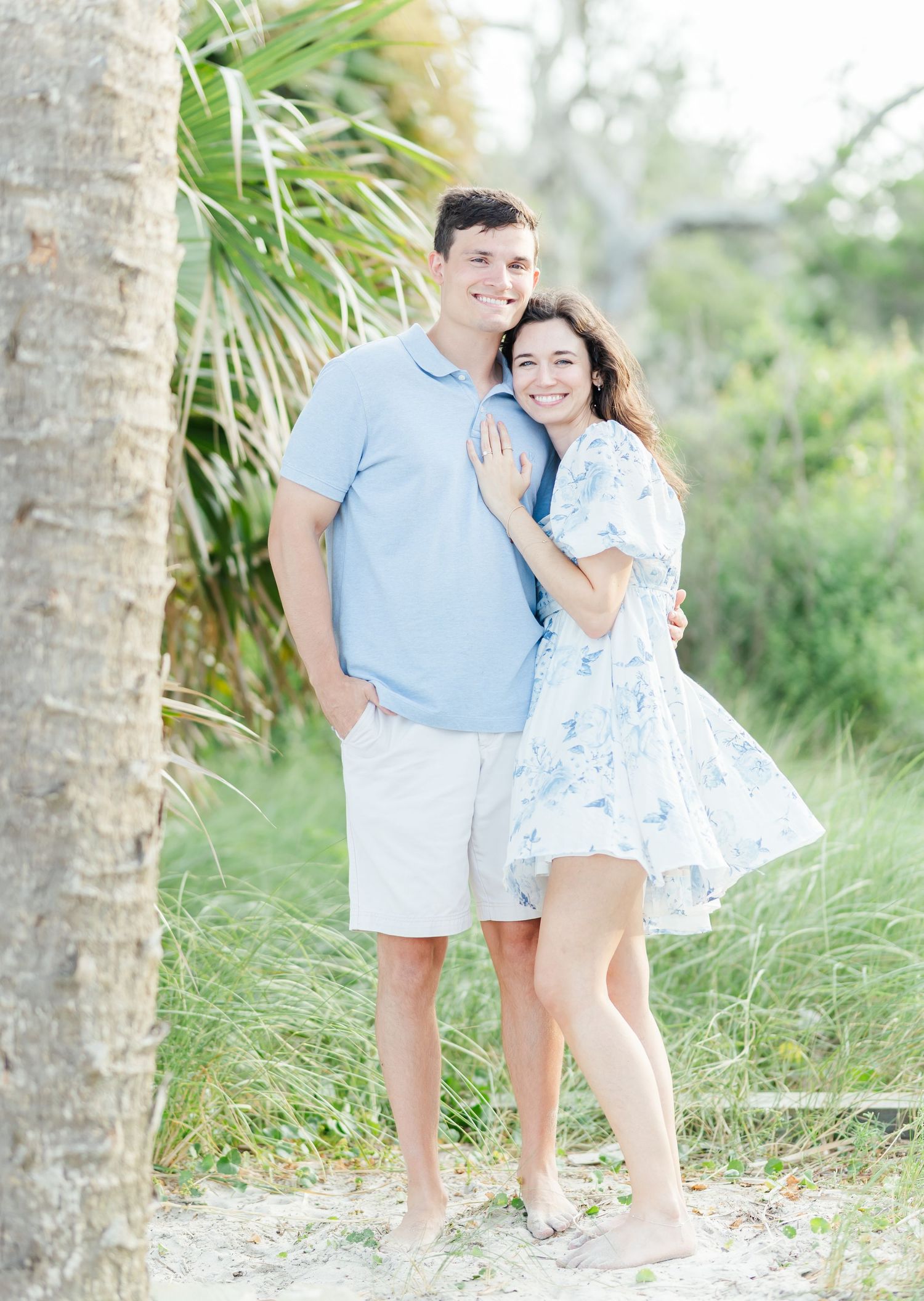 A joyful couple poses among palm trees in coordinated blue and white outfits.