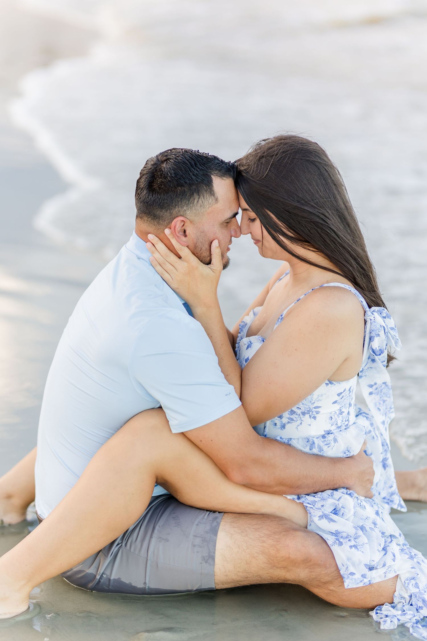 Romantic beach photoshoot sequence showing couple embracing on sandy shore in white and blue outfits.