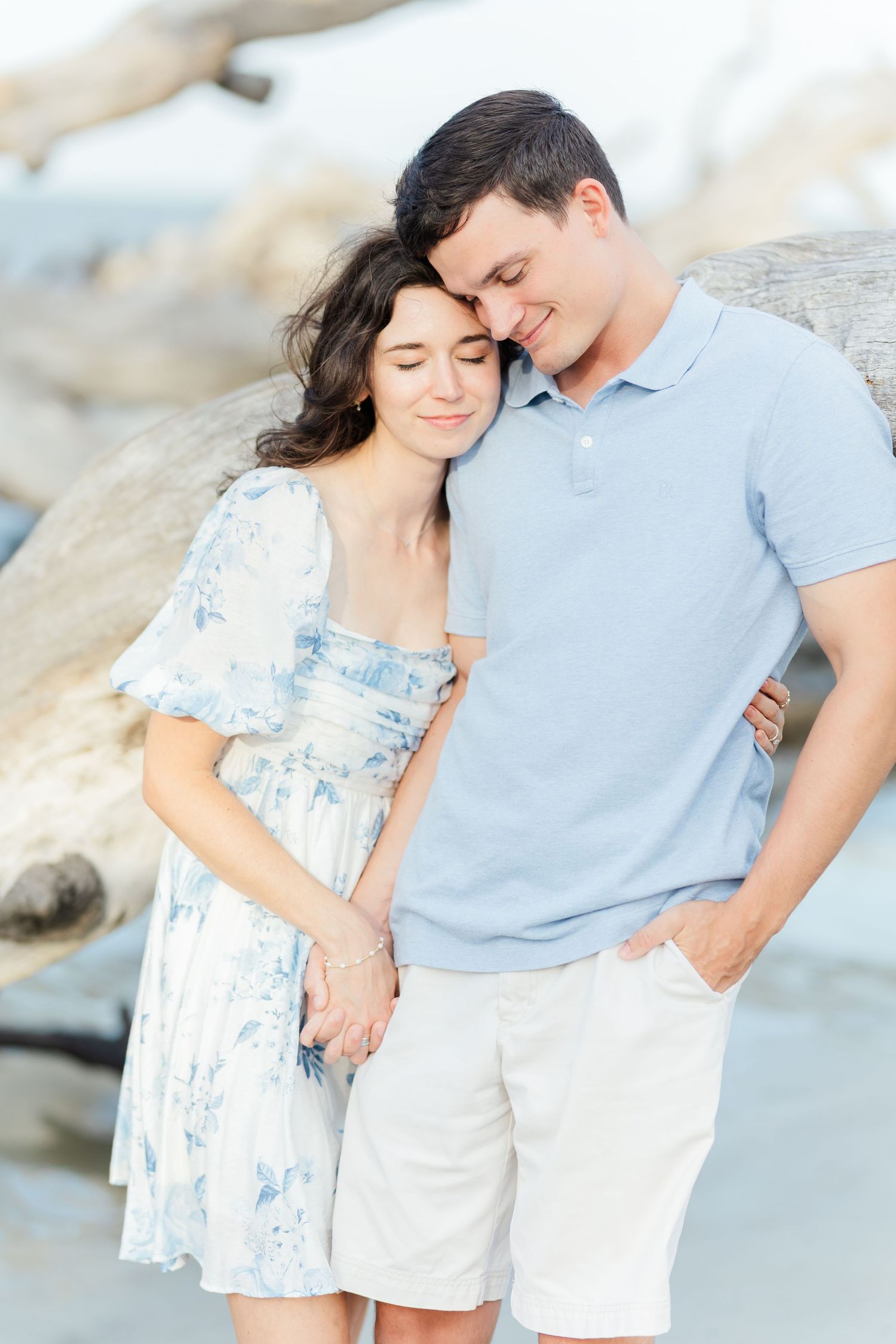 Intimate portrait of couple in blue and white attire sharing tender moment against blurred coastal background.