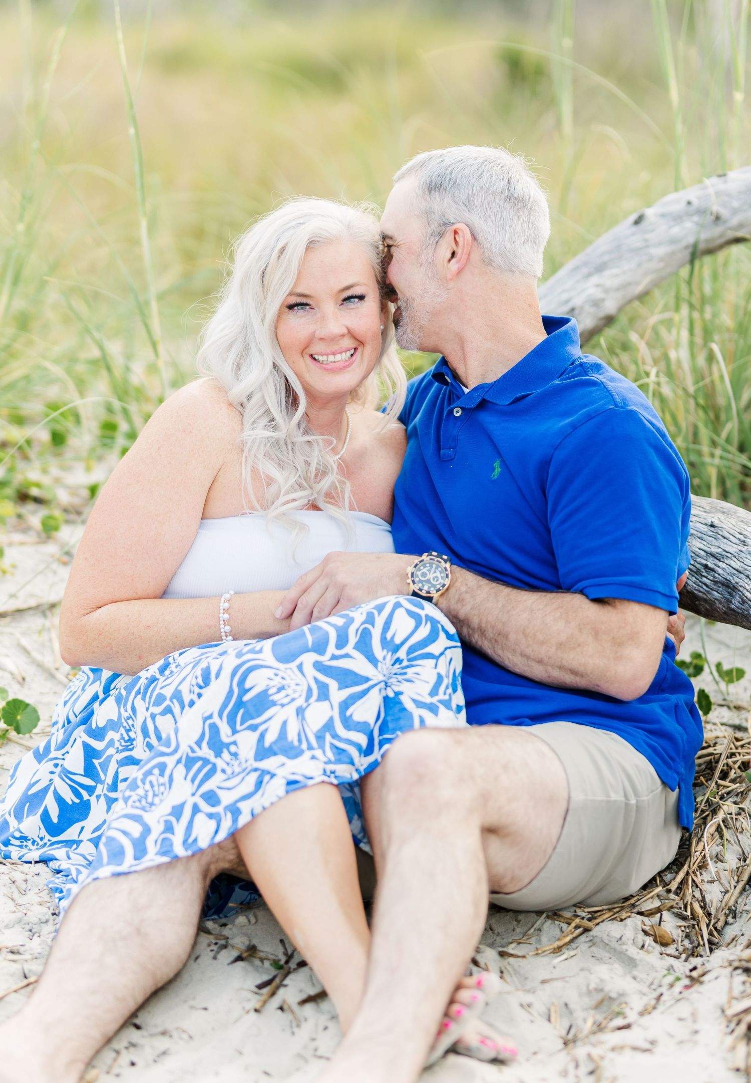 Romantic beach photoshoot with couple in matching blue and white outfits lounging on sandy shore.