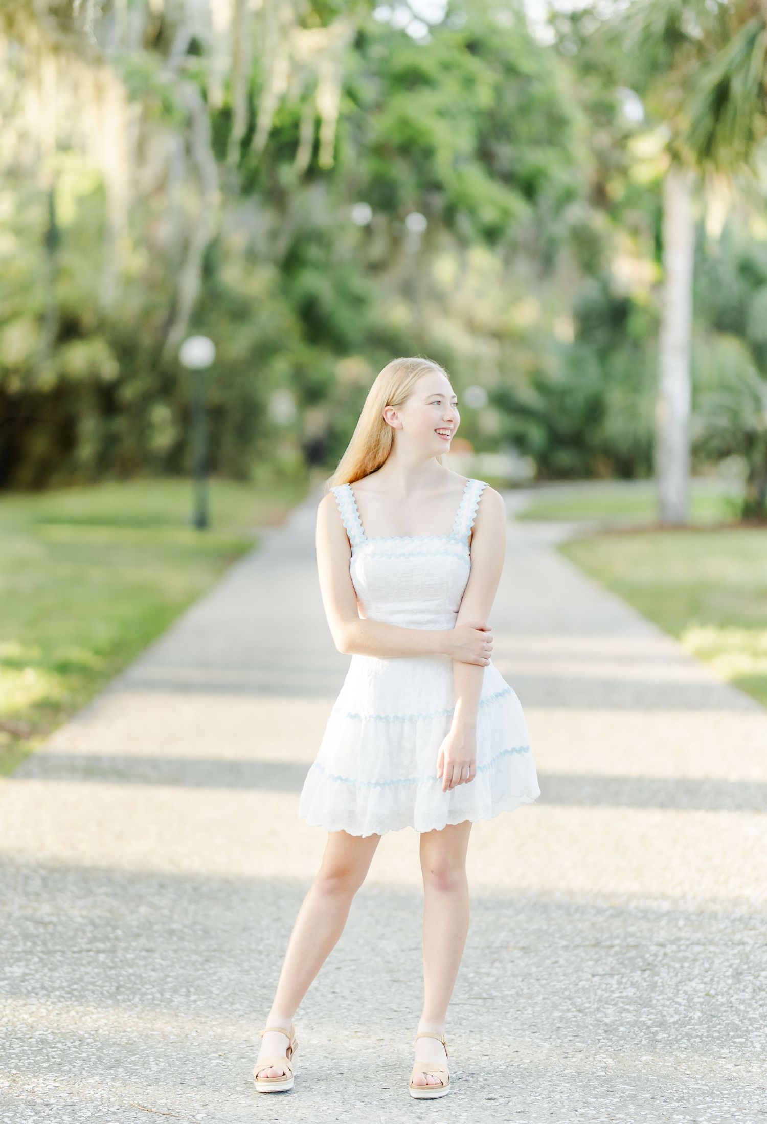 Person in white dress stands on gravel path surrounded by lush tropical garden landscaping.