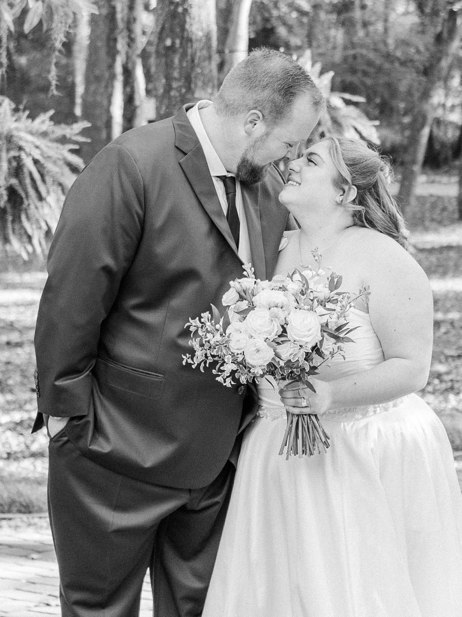 Black and white wedding party portrait showing formal attire and white floral bouquets in outdoor setting.