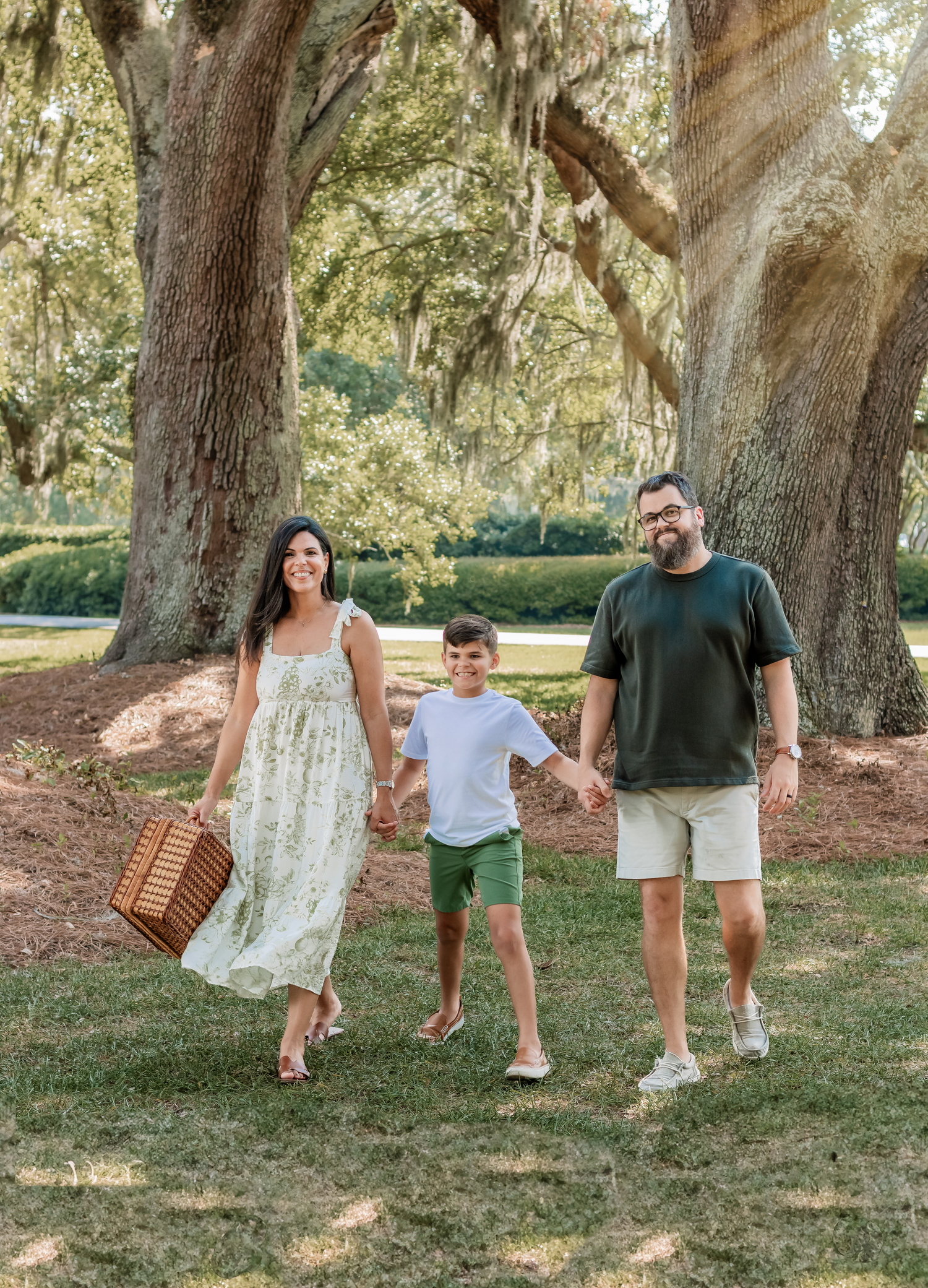 Family takes a casual stroll together under large oak trees draped with Spanish moss.