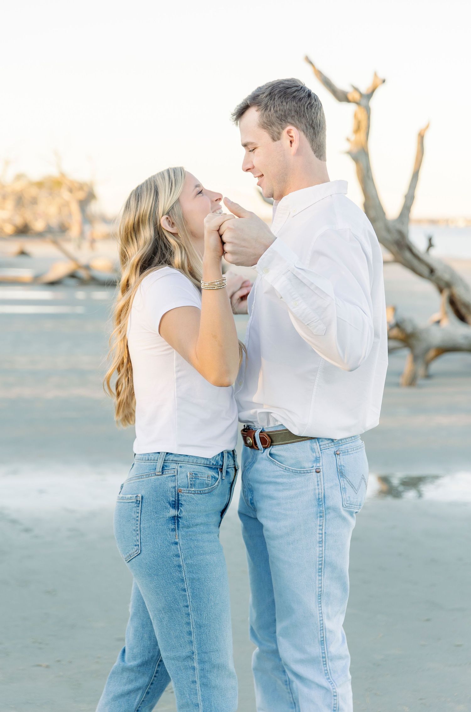 A couple in matching white tops and blue jeans share an intimate moment on a beach.