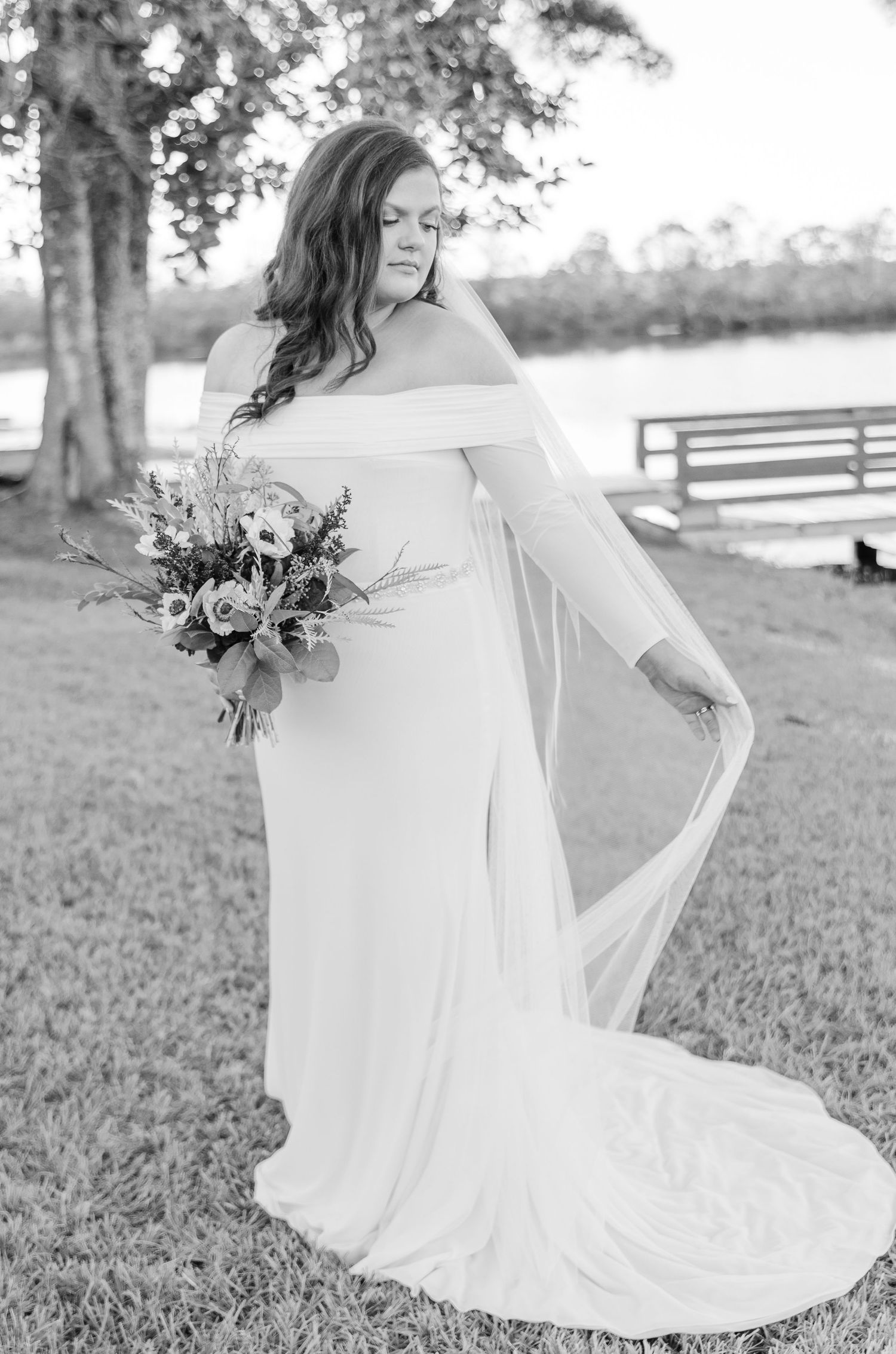 Elegant bridal portrait in off-shoulder gown with bouquet in outdoor setting.