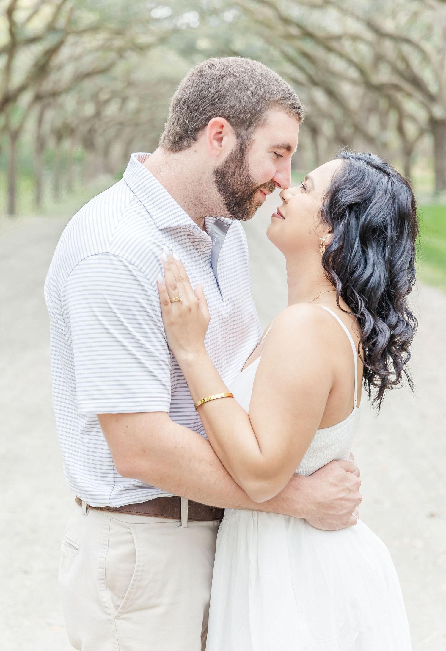 Romantic couple in white embracing outdoors under a canopy of trees.