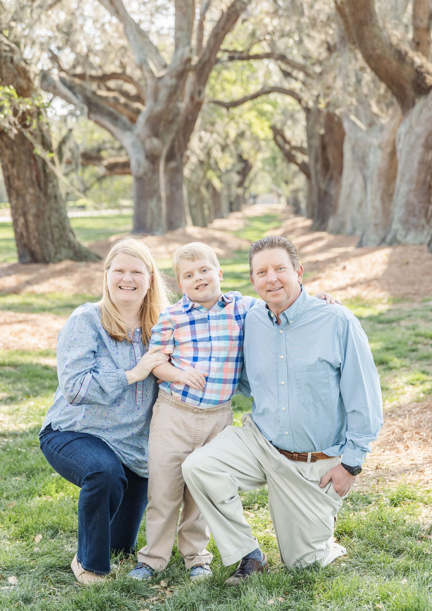 Family portrait in casual blue attire under canopy of oak trees.