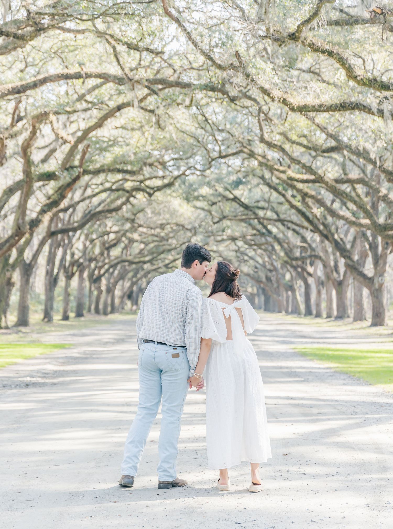 A romantic moment between a couple standing beneath an archway of oak trees.