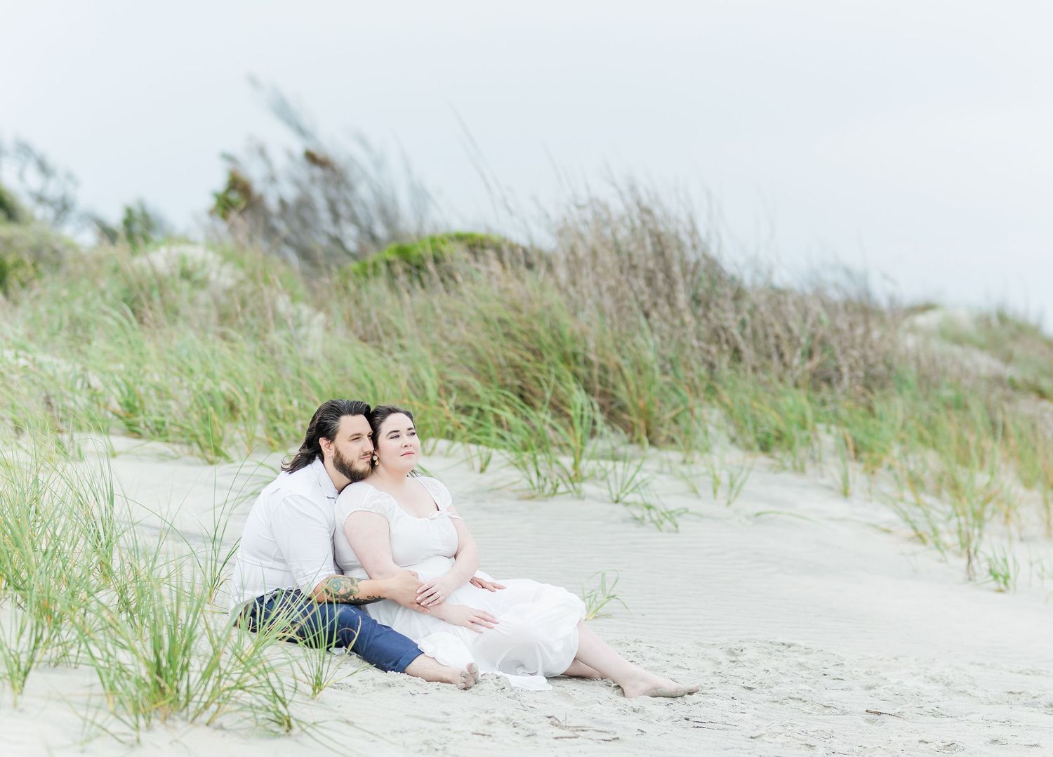 Two people sharing an intimate moment while sitting on a beach with dunes and sea grass.