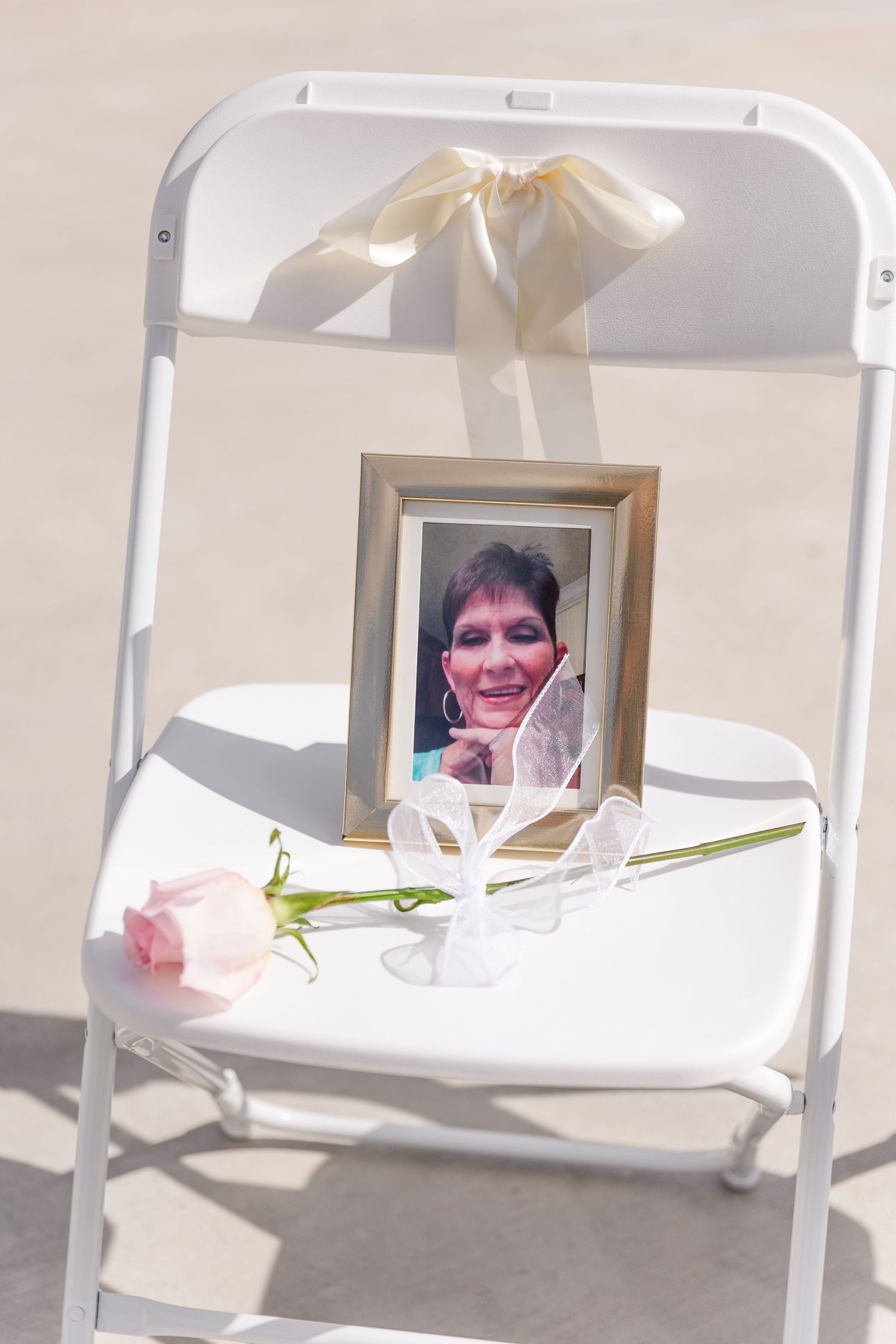 Memorial chair display with framed photograph and white ribbon at wedding ceremony.