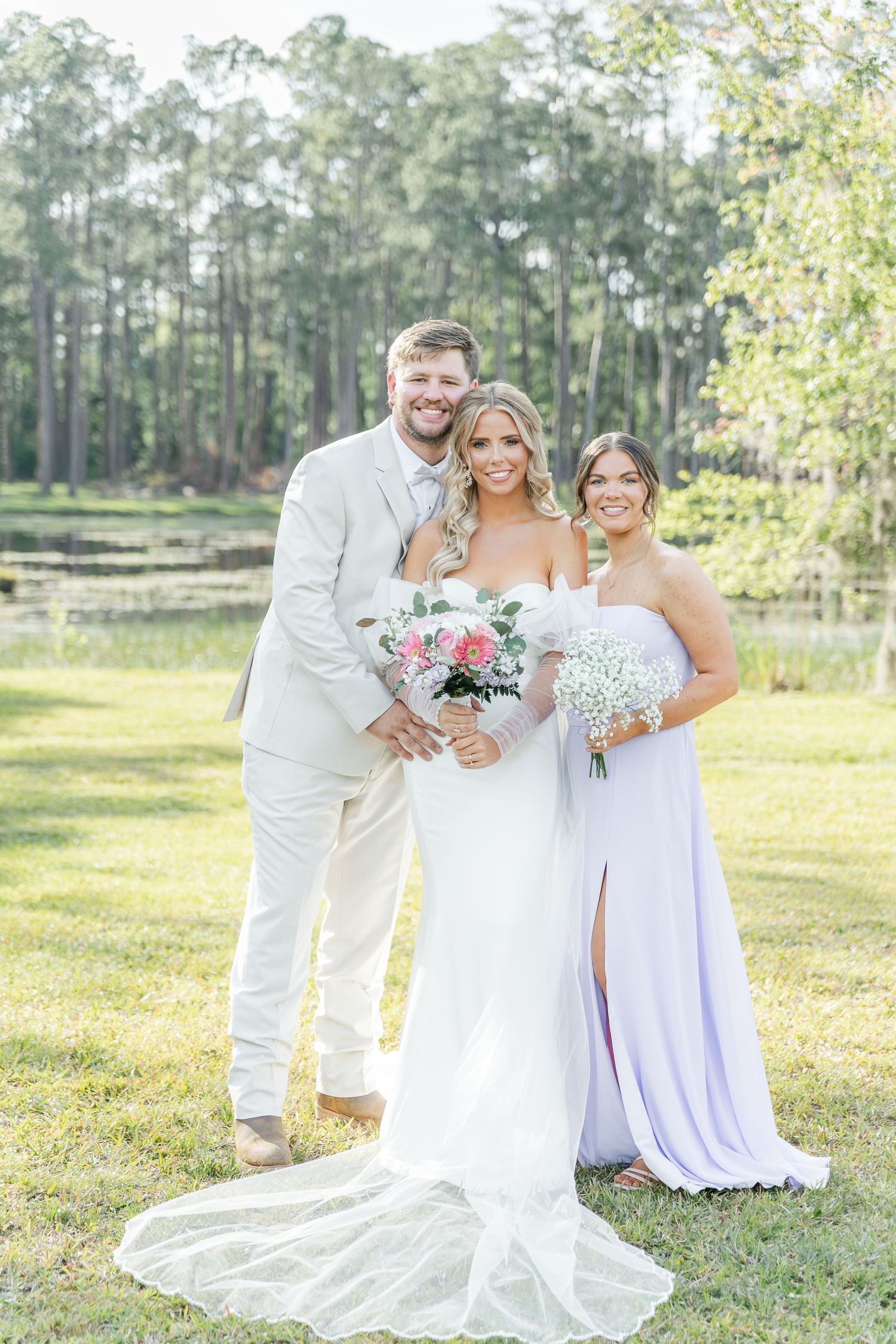 Sun-drenched wedding portrait with bridal party in white and lavender against pine forest backdrop.