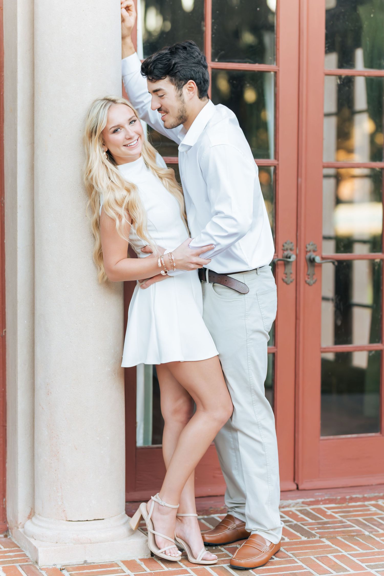 Engagement photos showing tender moments between a couple against red French doors and brick walls.