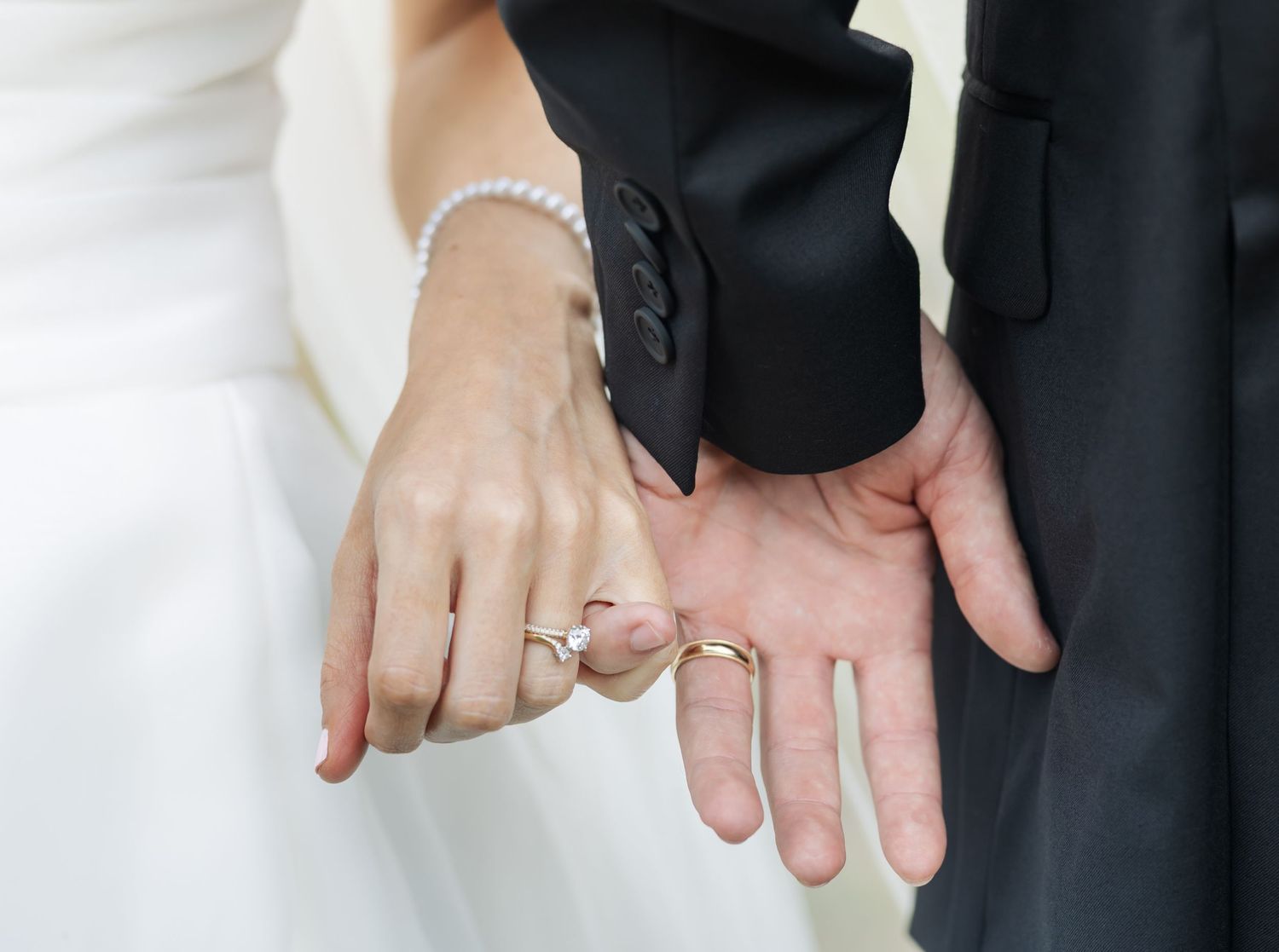 Three pairs of hands wearing wedding rings join together in a tender moment against a white background.