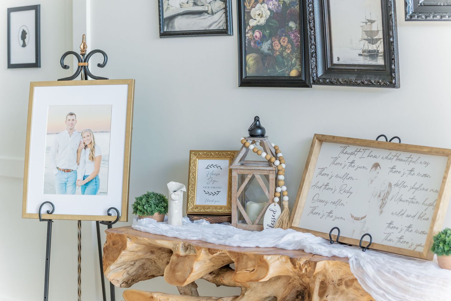 Wedding reception decor display with framed artwork, lantern, and wooden signs on a rustic table setting.