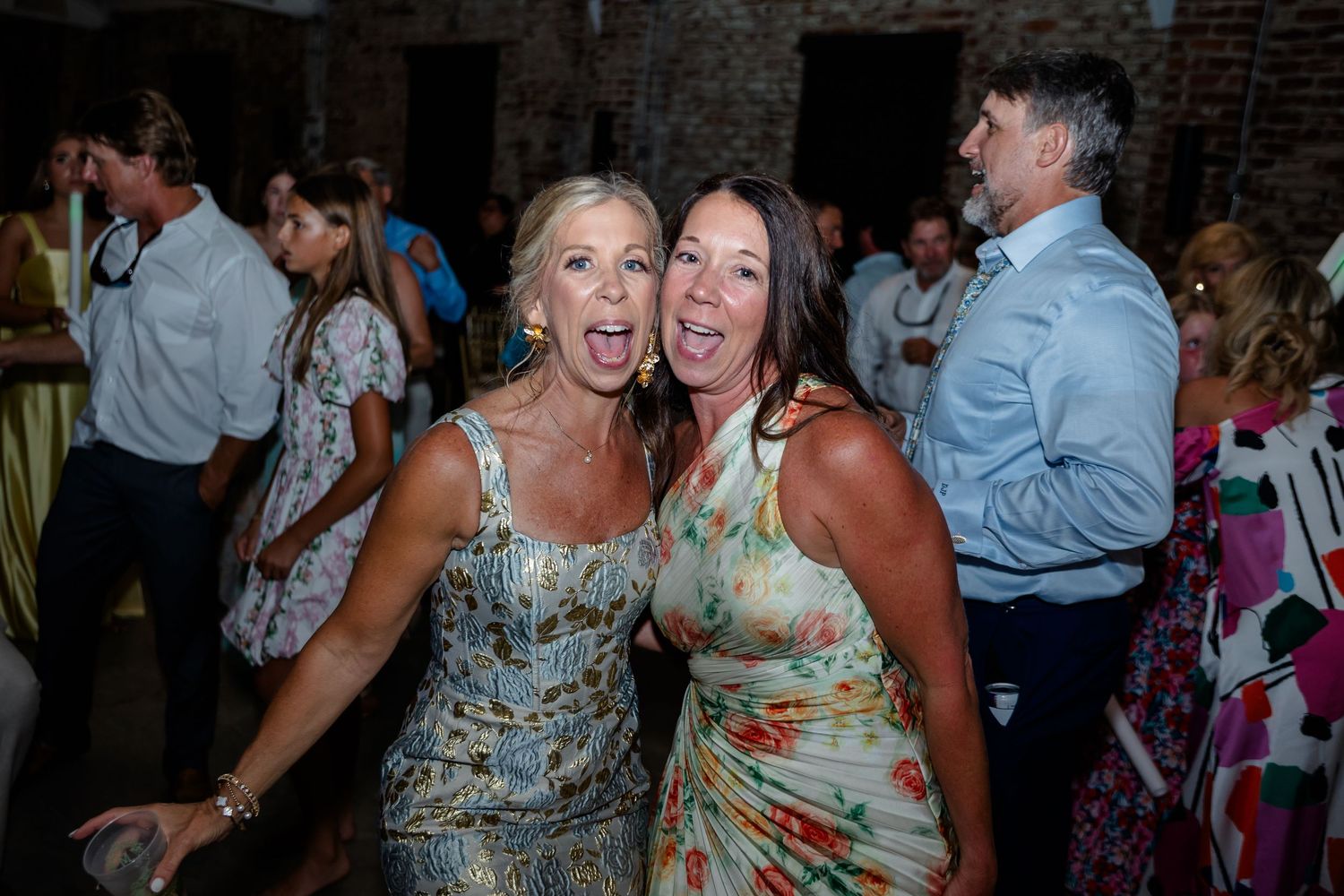 Lively wedding reception dance party in rustic brick venue with festive lighting.