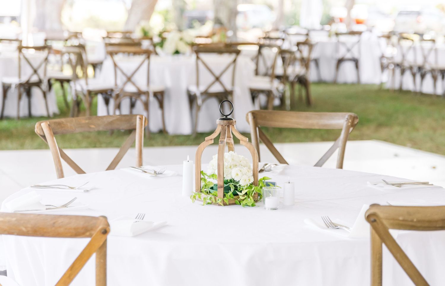 Elegant wedding reception setup with white chairs and rustic wooden cross-back chairs arranged in rows outdoors.
