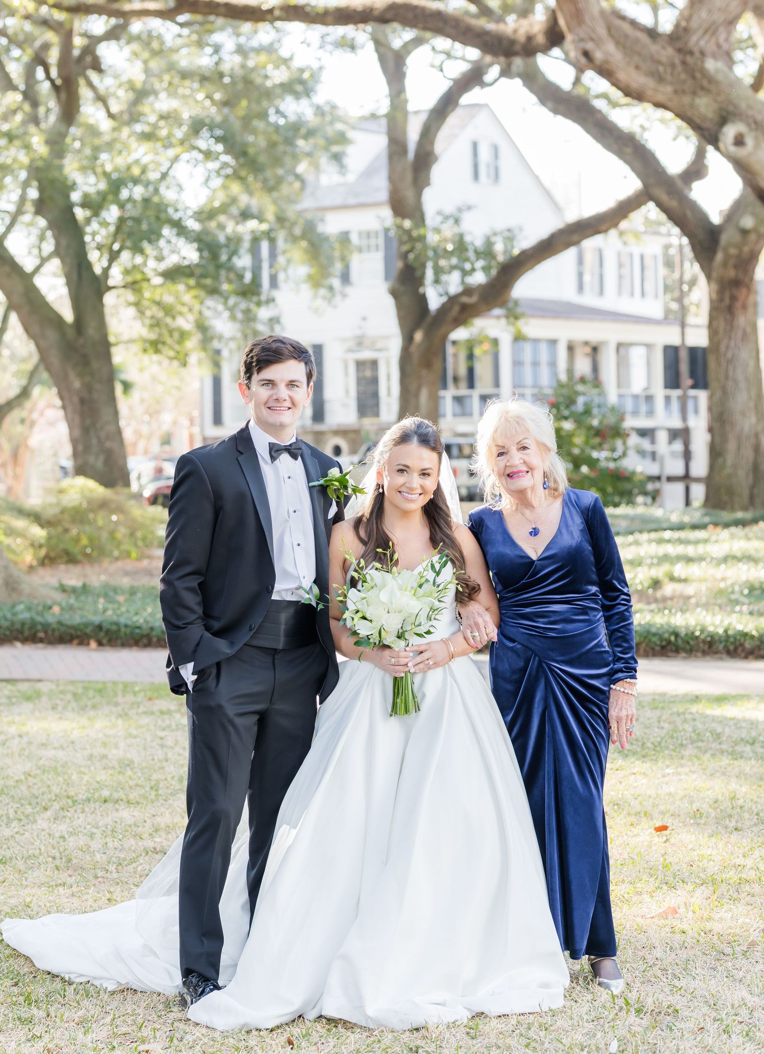 Wedding party poses together under oak trees in formal attire.