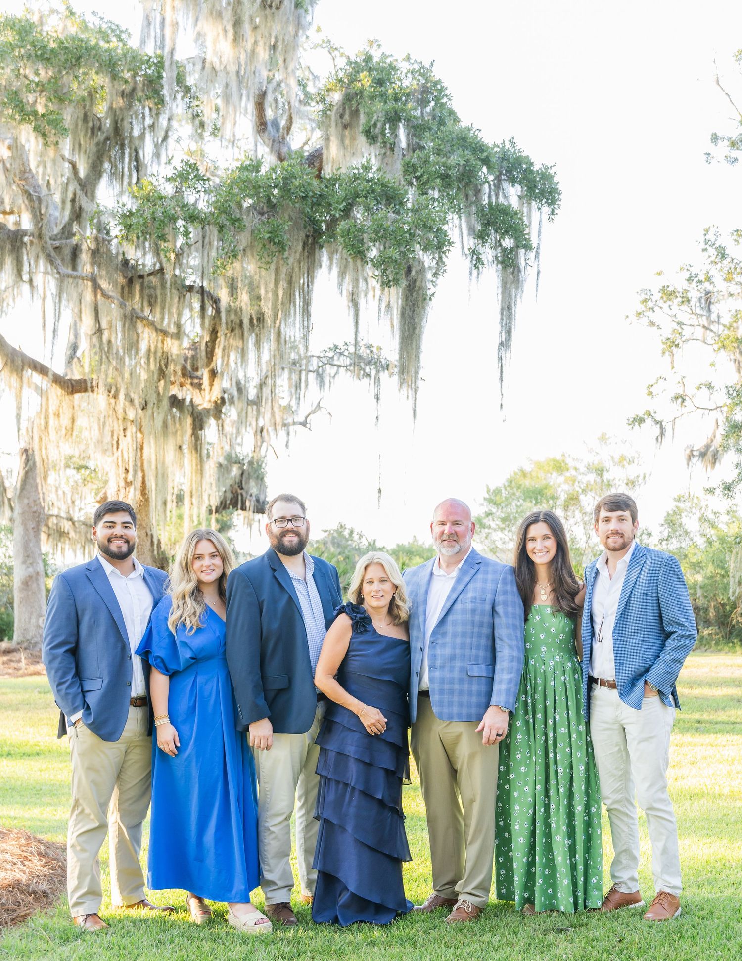 Wedding party in blue and green attire poses together outdoors under Spanish moss draped trees.