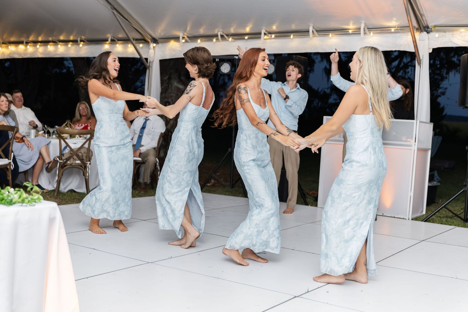 Wedding party members perform a choreographed dance routine at an outdoor reception.