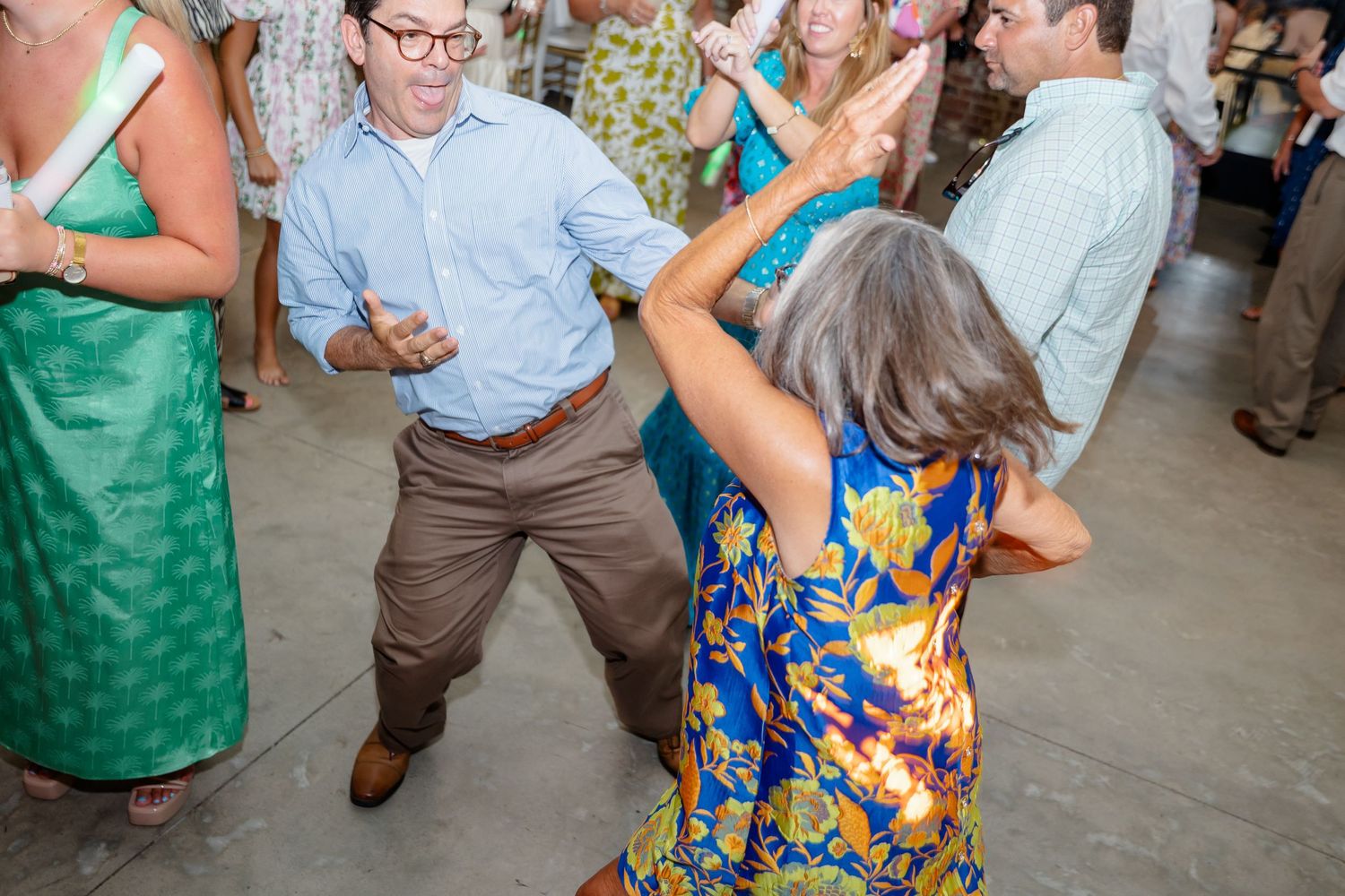 Wedding guests dancing in colorful summer attire at a rustic brick venue reception.
