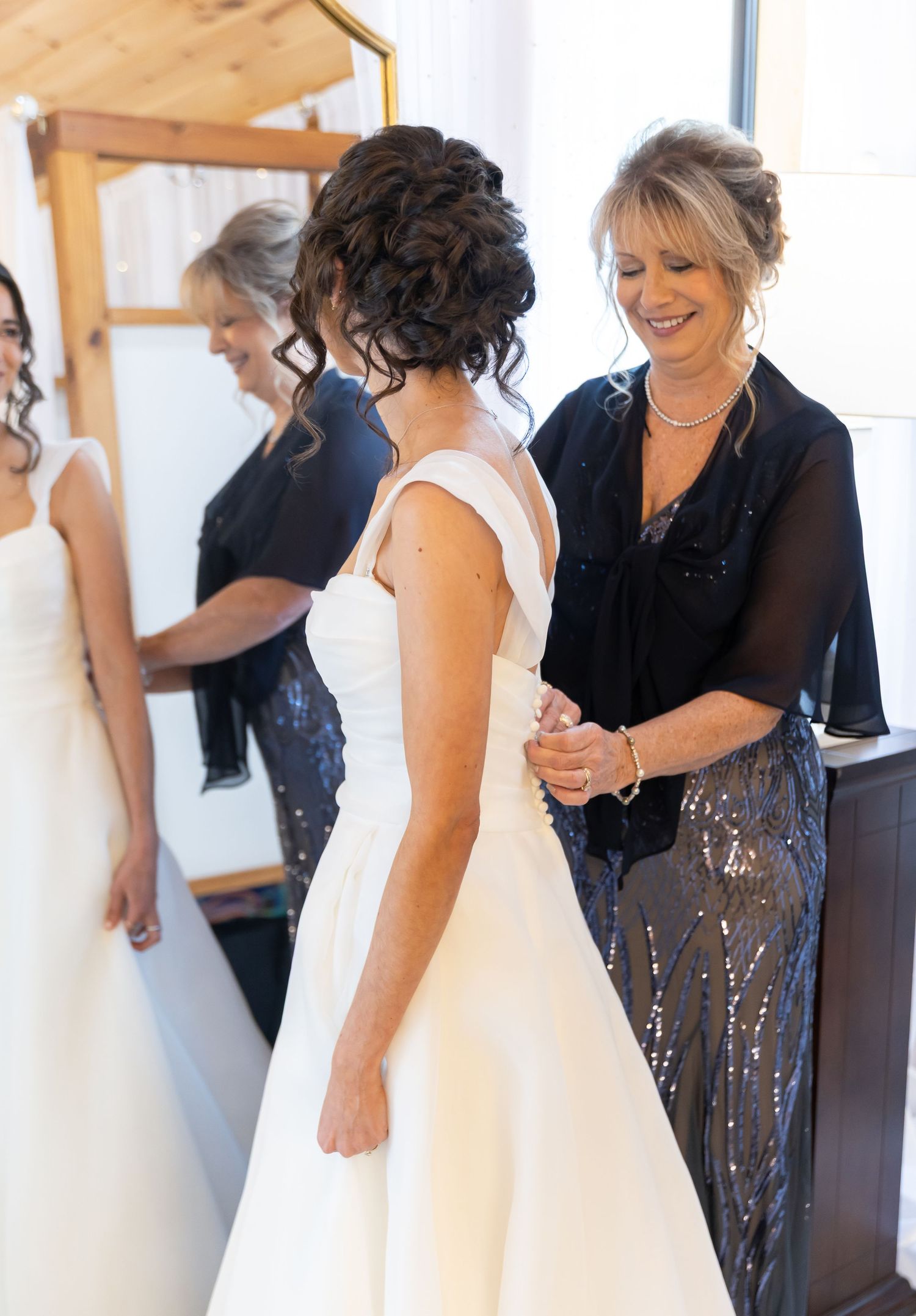 Wedding preparations showing bride being helped into dress by attendants in black dresses.