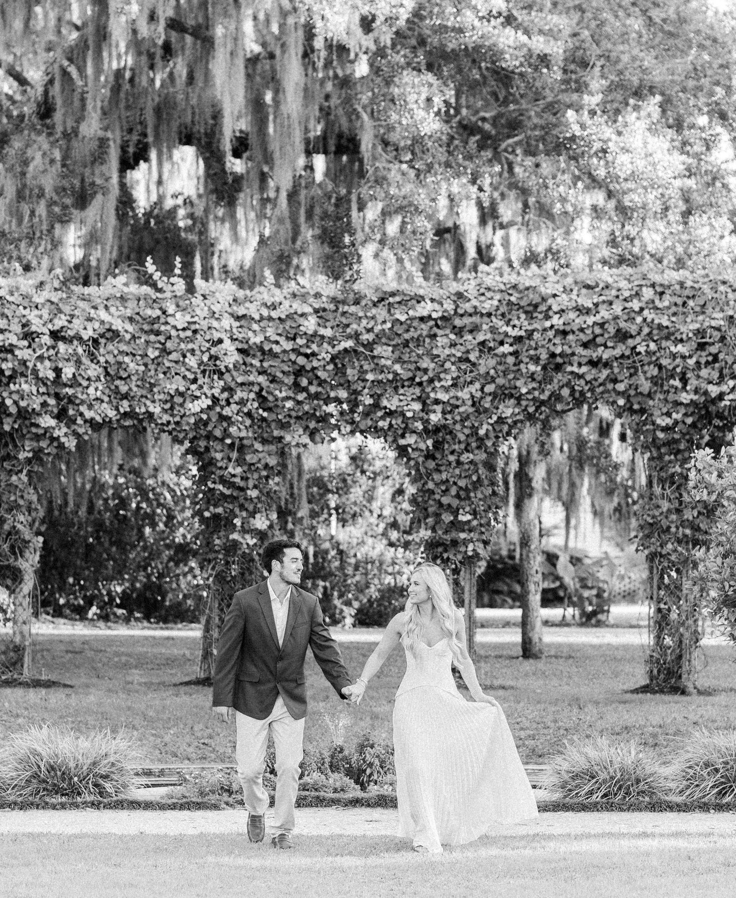 Black and white wedding photo series showing a couple walking together in a garden with Spanish moss overhead.
