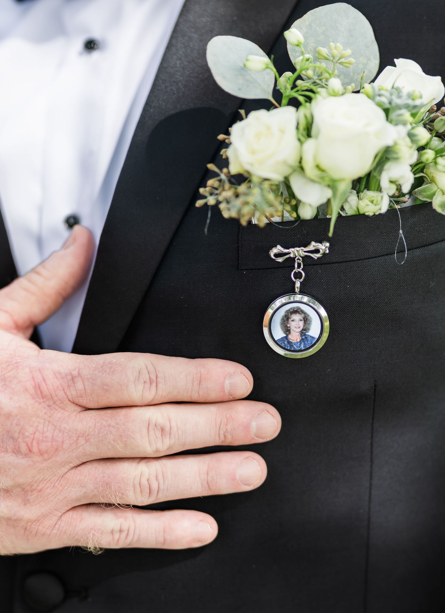 Wedding boutonniere with small white flowers and a memorial photo charm attached to honor loved ones.