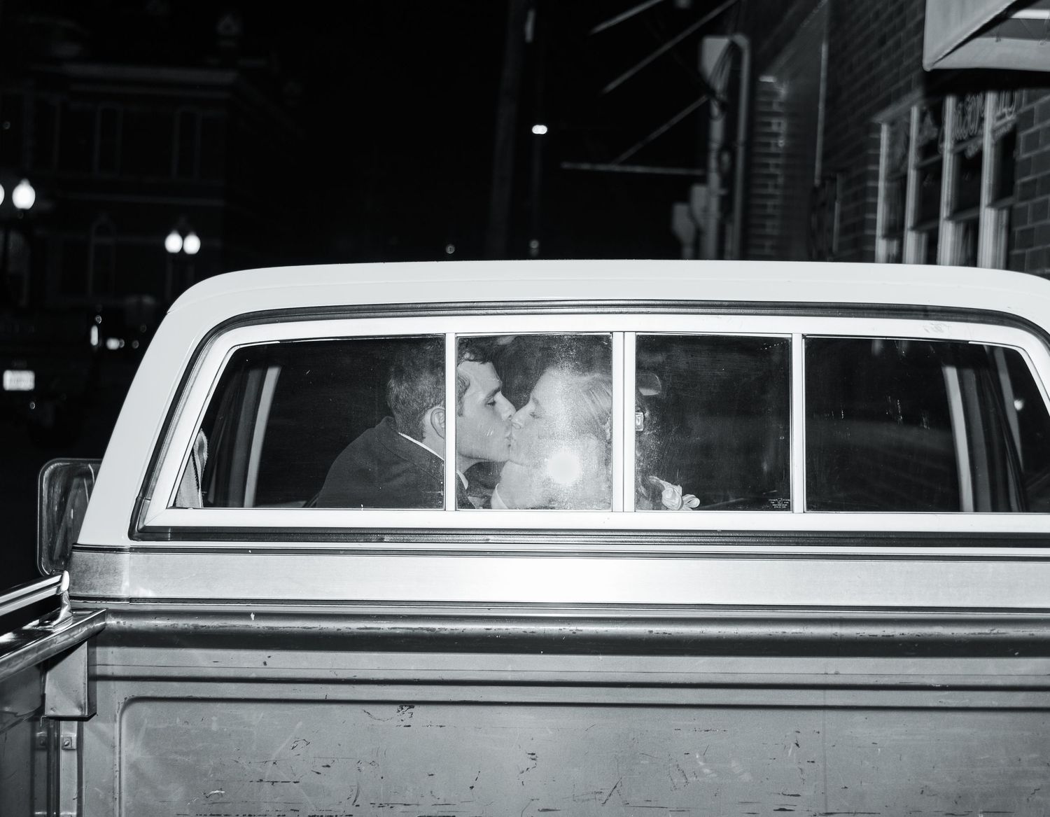 Black and white photo showing a row of vintage white limousines parked at night.