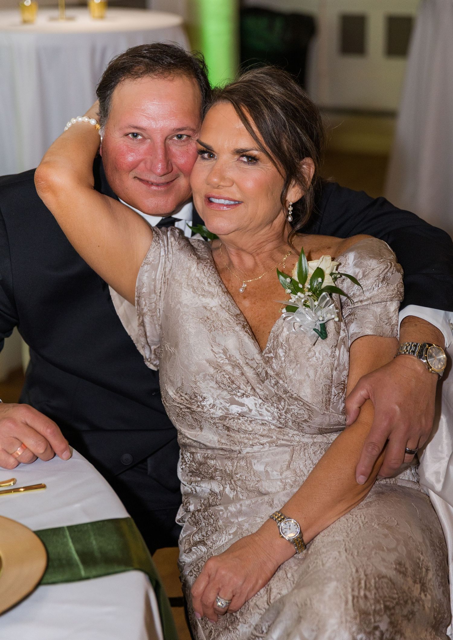 Couple in formal attire embracing warmly at wedding reception dinner table.