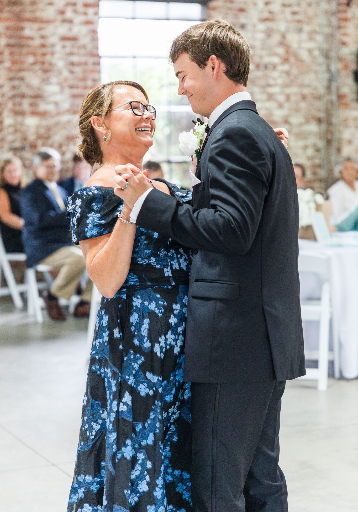 Mother and groom share a joyful dance together at wedding reception in rustic brick venue.