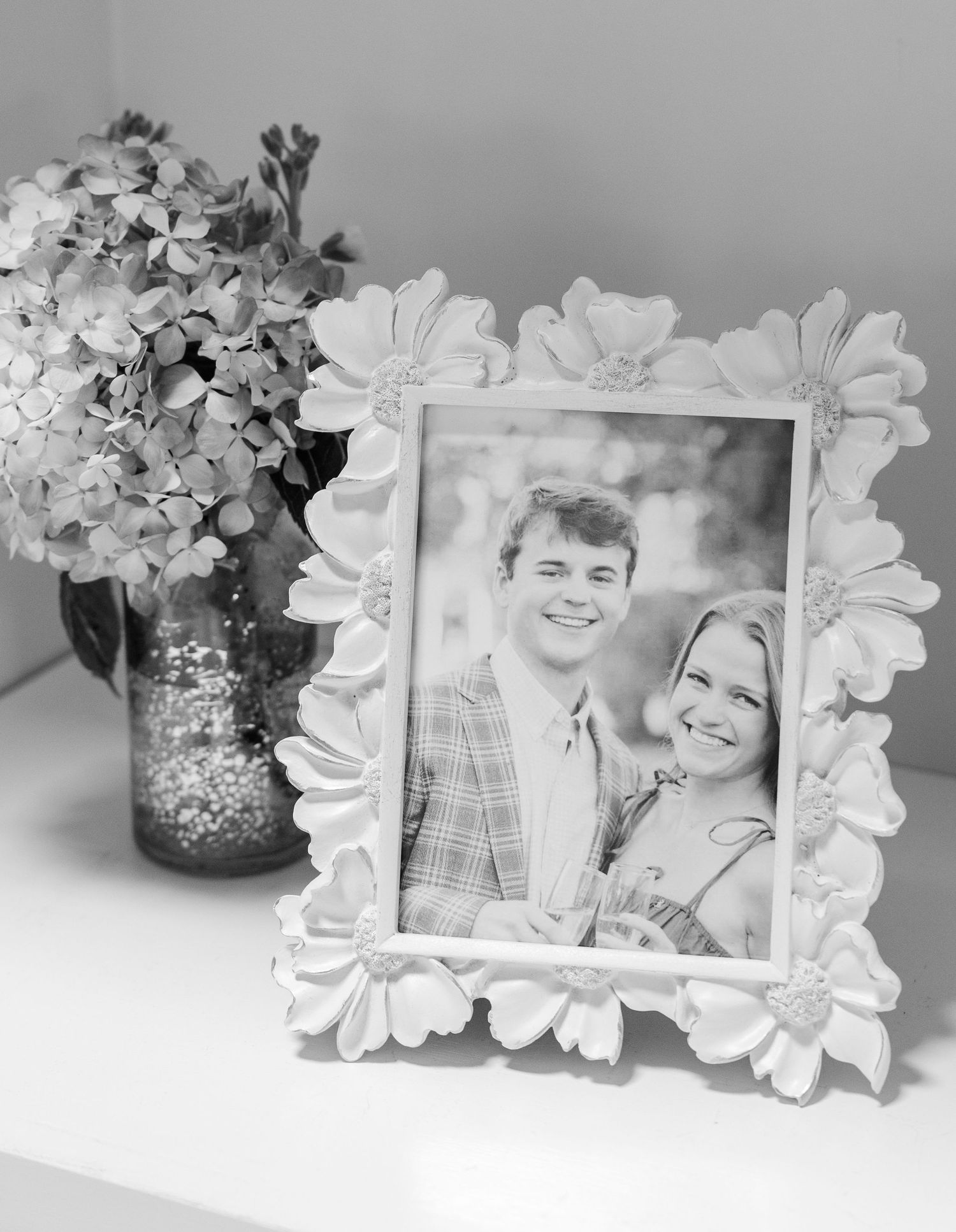 Black and white photo of smiling couple in decorative floral frame beside hydrangea arrangement.