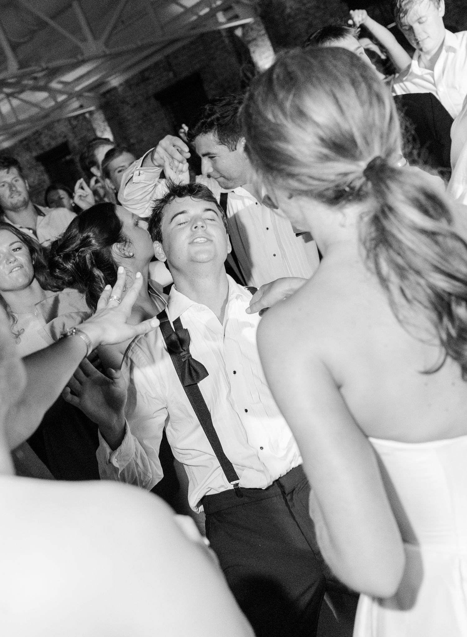 Black and white photo of groom dancing joyfully surrounded by guests at wedding reception.