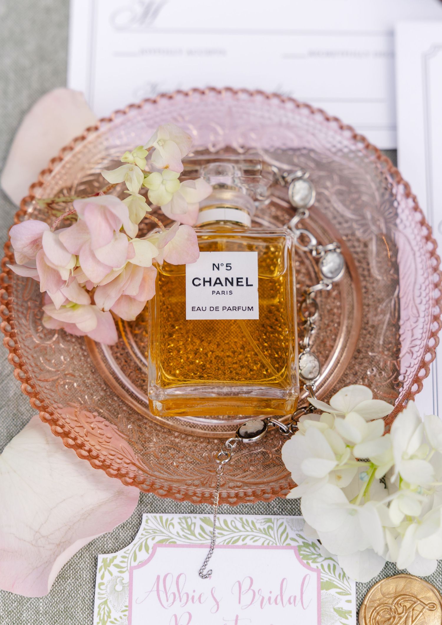 Chanel No. 5 Eau de Parfum bottle on a pink glass plate with hydrangeas and jewelry at a bridal party.
