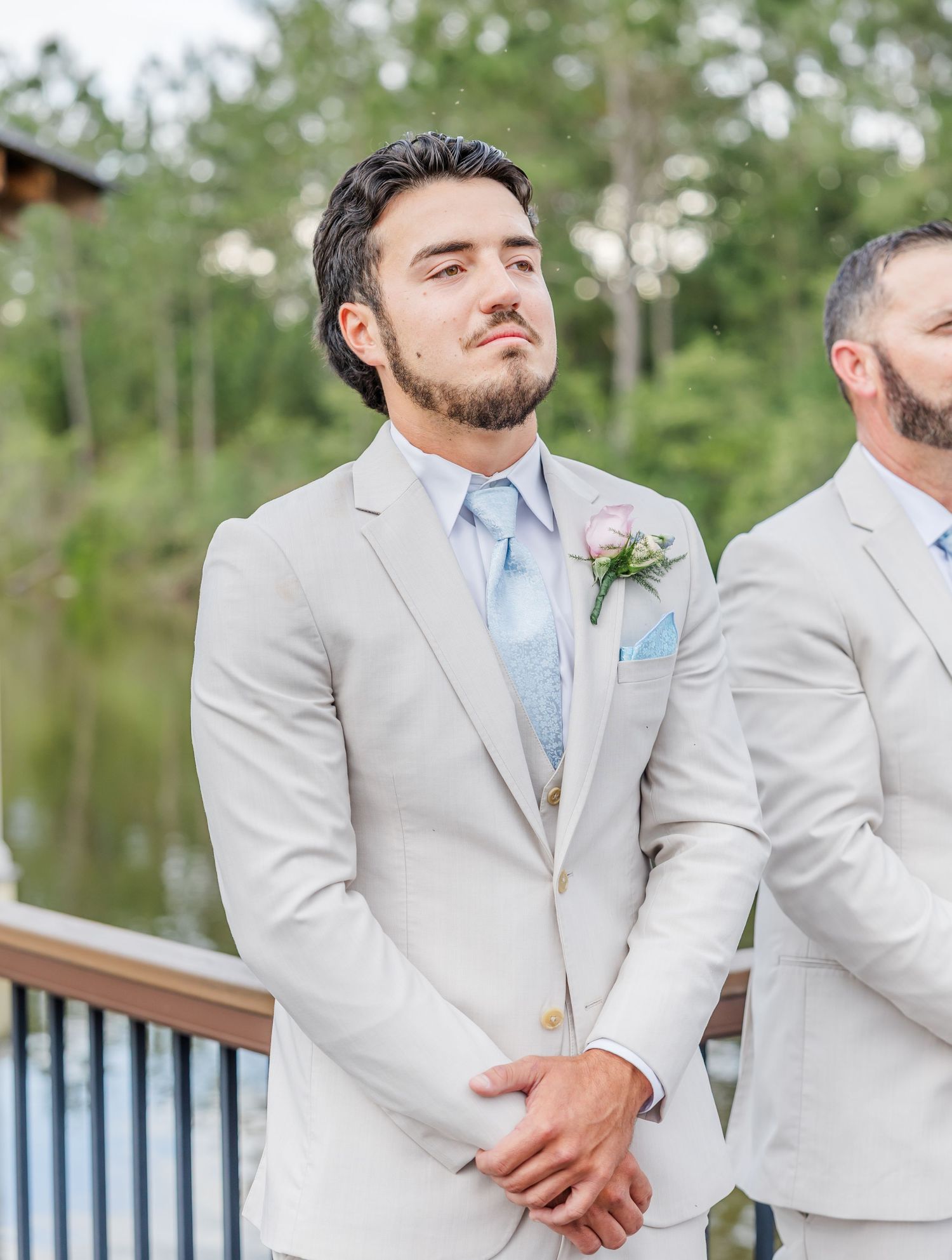 Groom in a light gray suit with blue tie and boutonniere looking up emotionally during wedding ceremony.