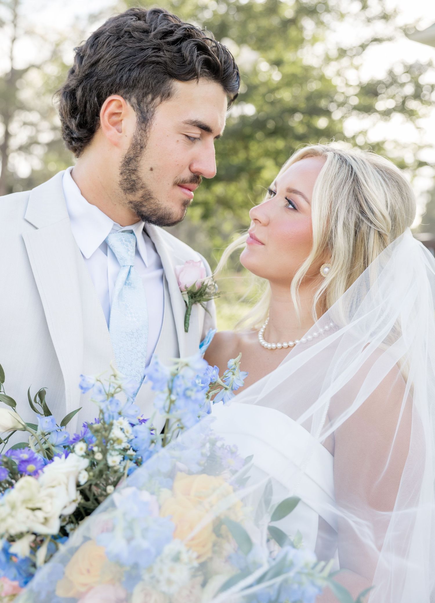 Romantic close-up of bride and groom gazing at each other with blue and white bouquet.