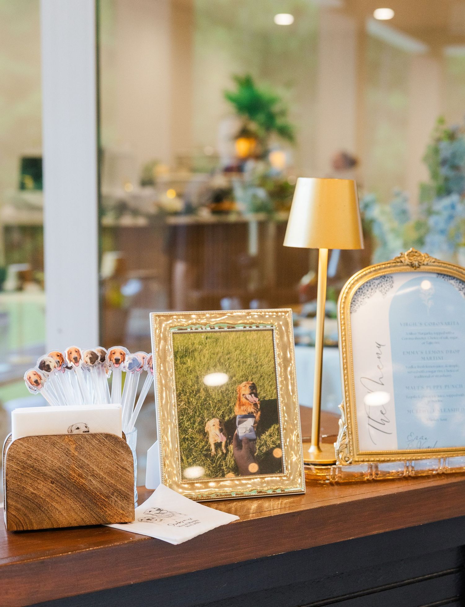 Elegant gold-framed photos and a brass lamp displayed on a wooden table at a wedding reception venue.