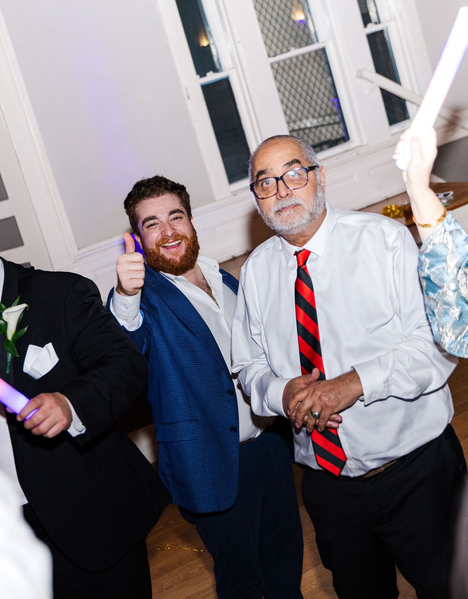 Two men smile and pose with thumbs up at a wedding reception.