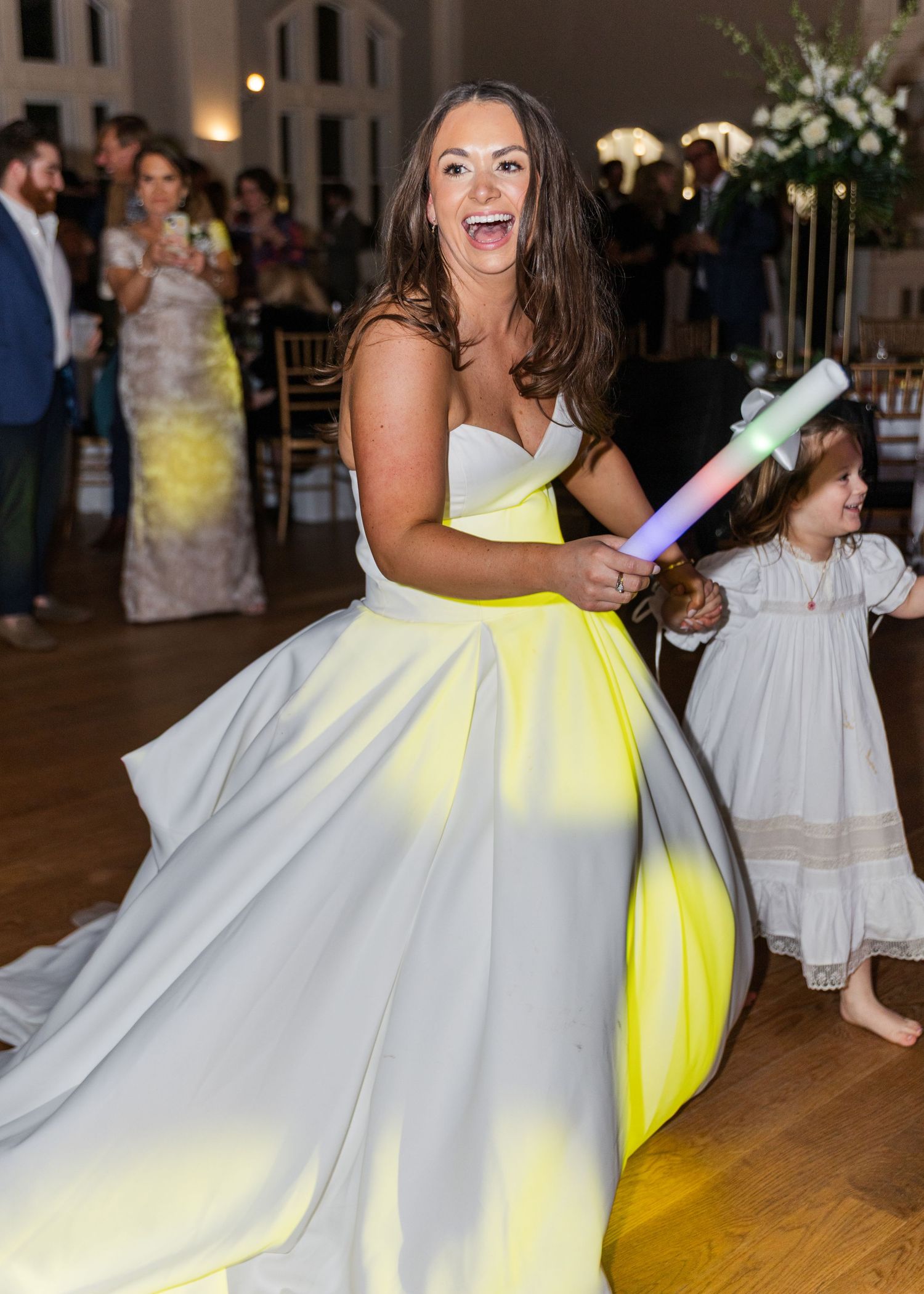 Excited bride in white ball gown dances with a glow stick at her wedding reception celebration.