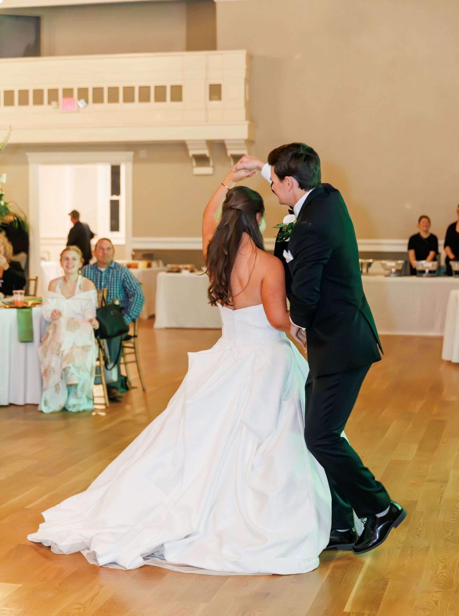 Bride and groom share their first dance at wedding reception while guests watch in elegant ballroom venue.