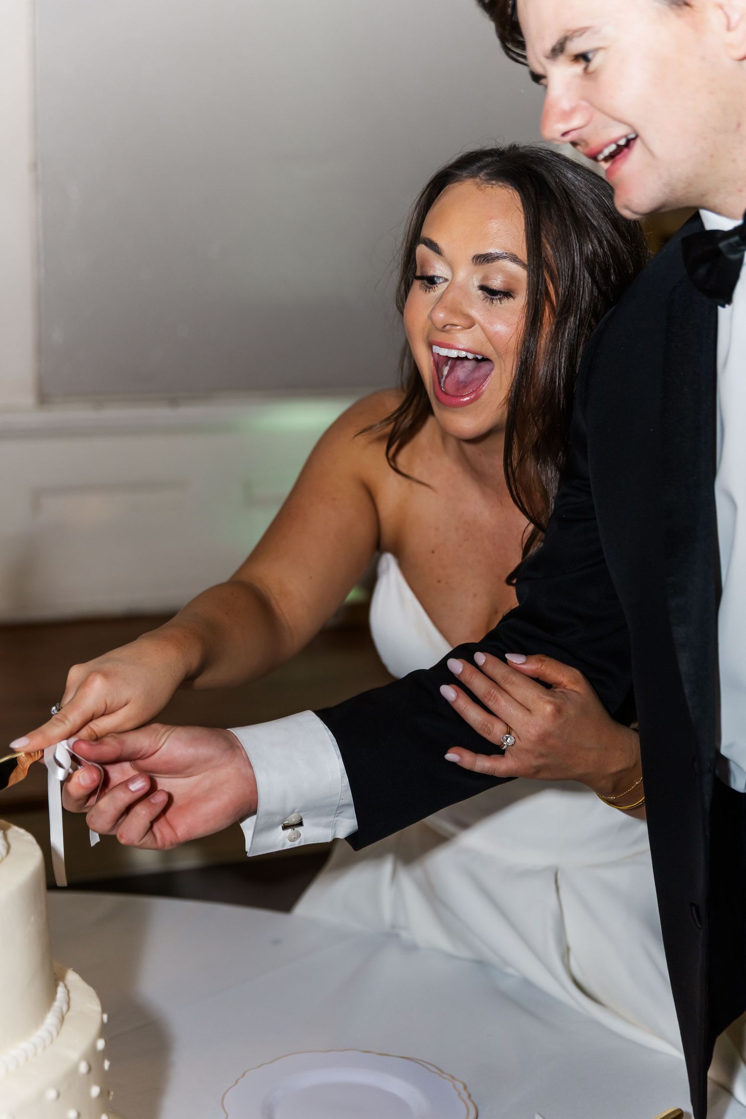 Bride and groom laughing while cutting their white wedding cake together during reception.