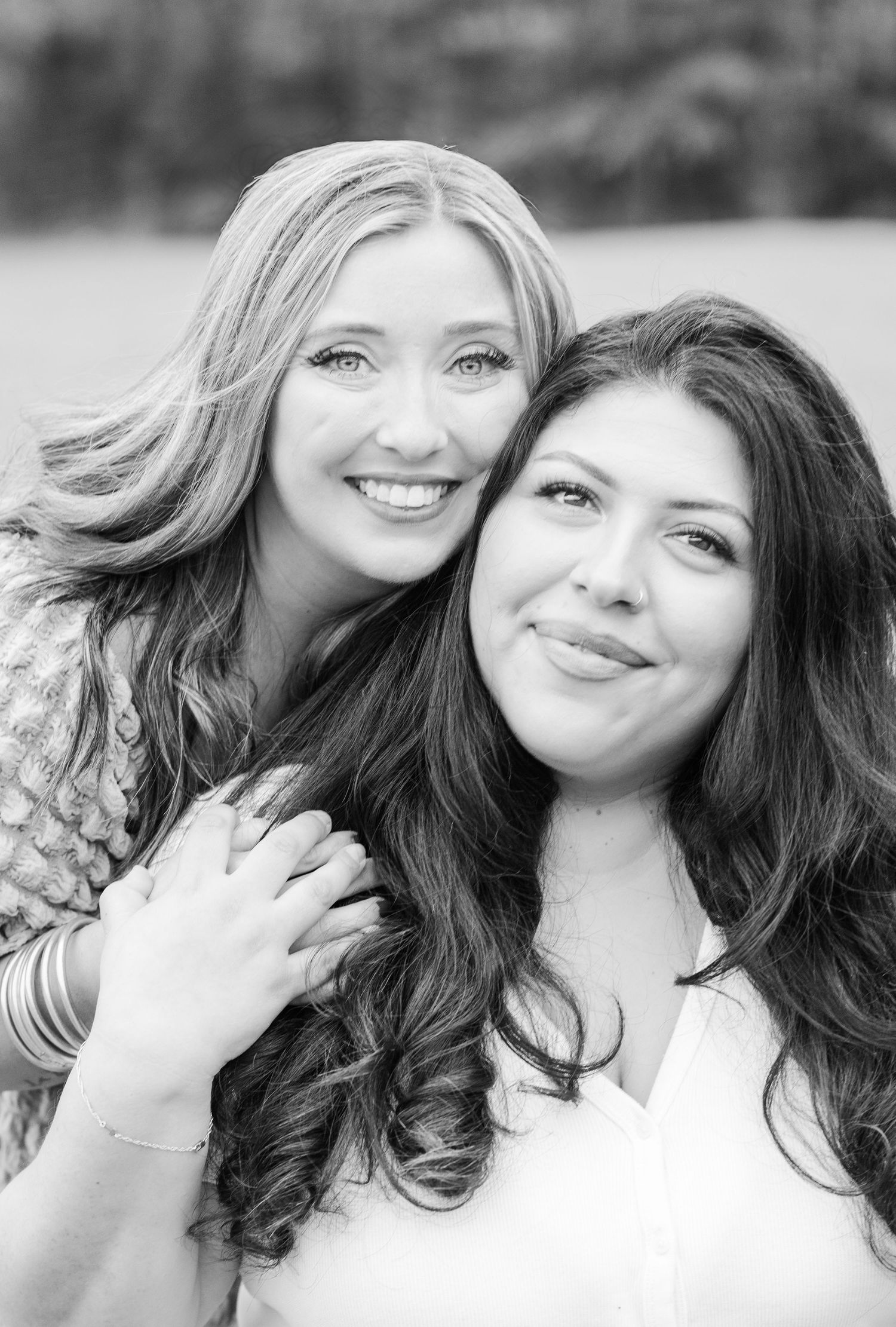 Two women with long hair pose together in a black and white close-up portrait showing warm smiles.