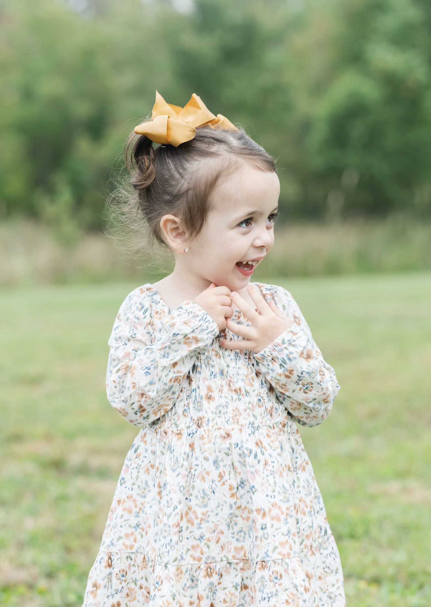 Child wearing floral print dress and mustard bow laughing joyfully outdoors.