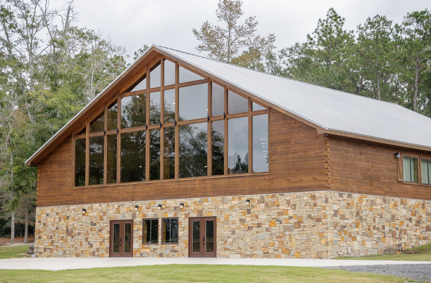 Modern rustic lodge with stone and wood exterior features large windows and peaked roofline in natural forest setting.