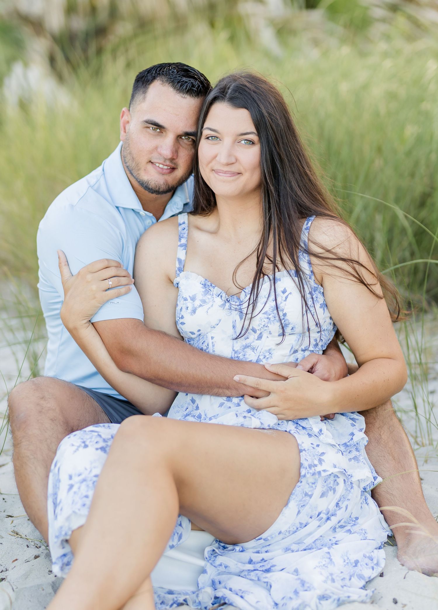 A couple poses intimately on sandy dunes with tall grass in a romantic outdoor photoshoot.