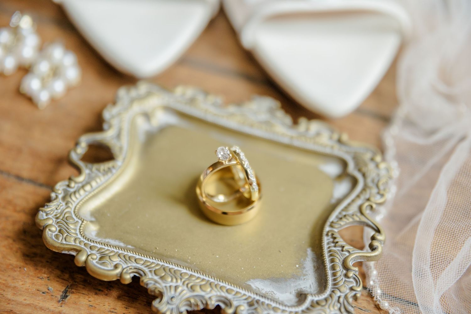 Wedding rings rest on an ornate vintage silver tray with gold accents on a wooden surface.